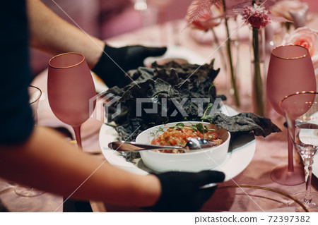 Waiter hands in gloves serving food for client. Food stylist decorate black food coronavirus protection in restaurant. 72397382