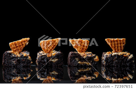 Brownies decorated with stroopwafel cookies on reflective dark black surface Brownies decorated with stroopwafel cookies on reflective dark black surface 72397651