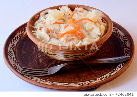 Sauerkraut with carrots in a clay plate and a fork are on the table. Sauerkraut with carrots in a clay plate and a fork are on the table. 72402041