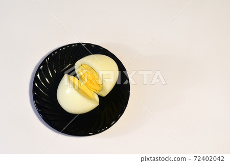 A peeled and cut chicken egg lies on a dark plate A peeled and cut chicken egg lies on a dark plate 72402042