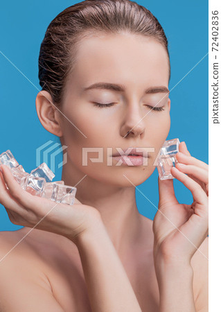 Beautiful woman applying ice cube treatment on blue background Beautiful woman applying ice cube treatment on blue background 72402836