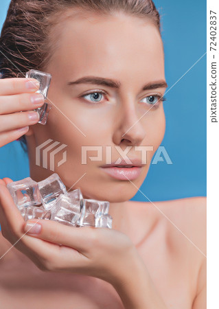 Beautiful woman applying ice cube treatment on blue background Beautiful woman applying ice cube treatment on blue background 72402837