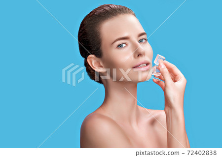 Beautiful woman applying ice cube treatment on blue background Beautiful woman applying ice cube treatment on blue background 72402838