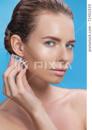Beautiful woman applying ice cube treatment on blue background Beautiful woman applying ice cube treatment on blue background 72402839