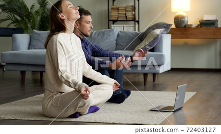 Online yoga practice. Couple meditating at home near laptop Online yoga practice. Couple meditating at home near laptop 72403127