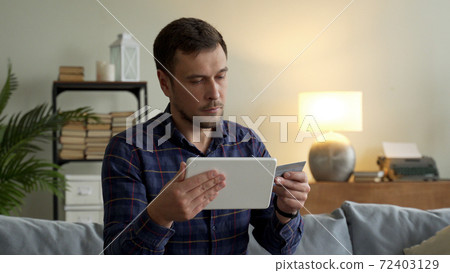 Man holding a credit card makes purchases online with the purchase of a tablet computer and payment. A man using a debit card to make a purchase. Man holding a credit card makes purchases online with the purchase of a tablet computer and payment. A man using a debit card to make a purchase. 72403129