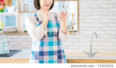 A young woman using a smartphone in the kitchen A young woman using a smartphone in the kitchen 72403839