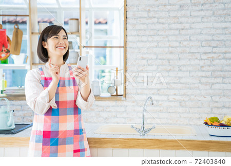 A young woman using a smartphone in the kitchen 72403840