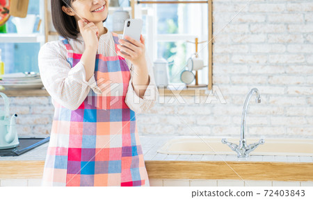 A young woman using a smartphone in the kitchen A young woman using a smartphone in the kitchen 72403843