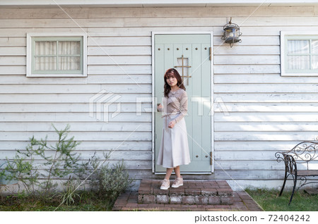 A young woman standing in front of the entrance door of a Western-style building 72404242