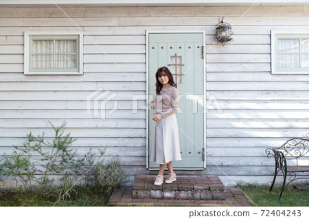A young woman standing in front of the entrance door of a Western-style building 72404243