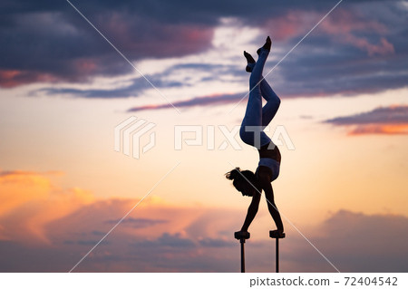 Flexible female circus Artis keep balance and doing contortion on the rooftop against dramatic sunset and cityscape. Motivation, passion and achievement concept  72404542