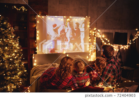 family mother father and children watching projector, film, movies with popcorn in   christmas evening   at home. 72404903