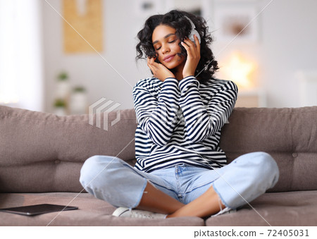 Ethnic female listening to music on sofa. 72405031