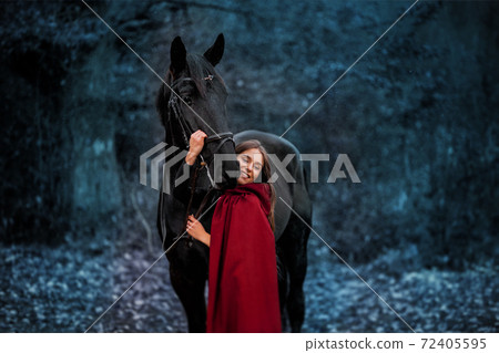 Fabulous portrait of a beautiful young lady with long brown hair, suite with red or burgundy cloak with her black horse in winter Fabulous portrait of a beautiful young lady with long brown hair, suite with red or burgundy cloak with her black horse in winter 72405595