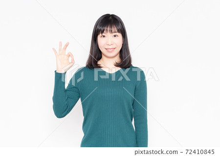 Woman standing in front of white background and making an OK gesture 72410845