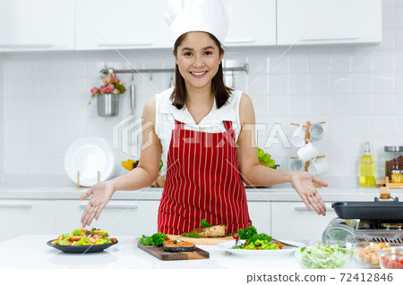 Happy Asian woman chef with red apron standing in the kitchen. Concept woman cooking at home. 72412846