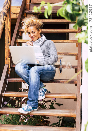 Happy trendy caucasian beautiful woman use online computer with internet connection to work in the garden at home like an alternative office - smart work technology people 72412957