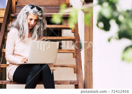 Happy trendy caucasian senior woman use online computer with internet connection to work in the garden at home like an alternative office - smart work technology people Happy trendy caucasian senior woman use online computer with internet connection to work in the garden at home like an alternative office - smart work technology people 72412958