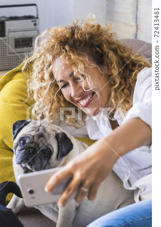 People and dog stay at home concept with cheerful happy beautiful adult woman taking selfie picture with her best friend pug animal - people enjoy technology and sharing with friends 72413481