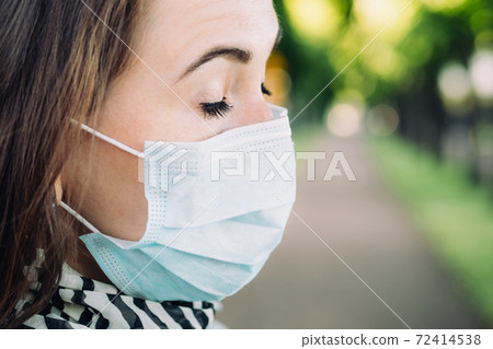 Portrait of a thirty-year-old Caucasian girl in a medical mask with closed eyes on a park background Portrait of a thirty-year-old Caucasian girl in a medical mask with closed eyes on a park background 72414538