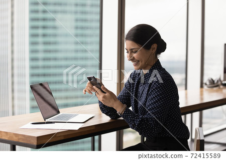 Smiling Indian woman look at cellphone screen texting Smiling Indian woman look at cellphone screen texting 72415589