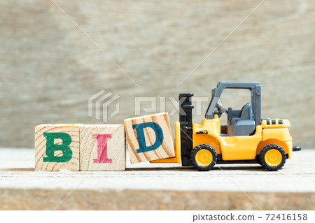 Toy forklift hold letter block d to complete word bid on wood background Toy forklift hold letter block d to complete word bid on wood background 72416158