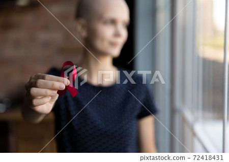 Close up dreamy hairless woman holding awareness red ribbon 72418431