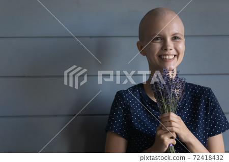 Head shot smiling hairless woman cancer patient holding flowers 72418432