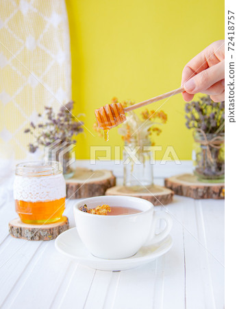 Glass cup of tea with linden in natural organic herbs and a jar of honey on a white wooden table. Glass cup of tea with linden in natural organic herbs and a jar of honey on a white wooden table. 72418757