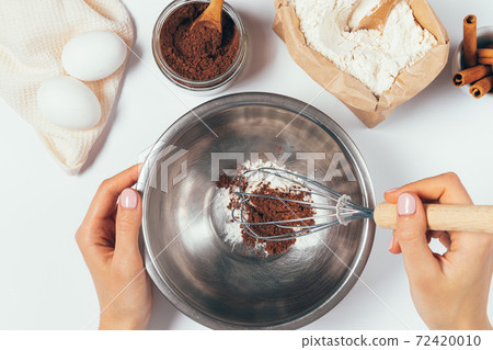 Top view of female hands whisk flour and cocoa powder Top view of female hands whisk flour and cocoa powder 72420010