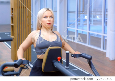 Sportive woman is doing exercises for spine muscles on block rowing machine. 72420500