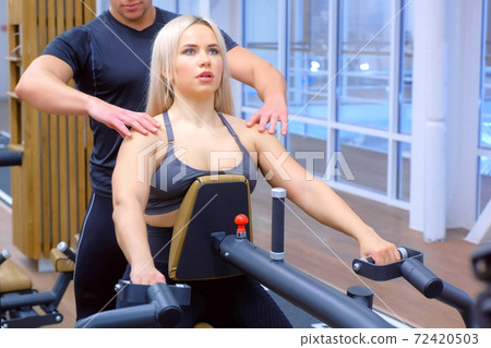 Sportive woman is doing exercises for spine muscles on block rowing machine. Sportive woman is doing exercises for spine muscles on block rowing machine. 72420503