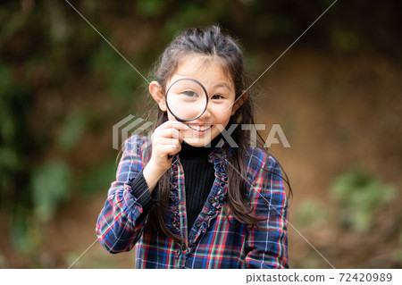 A girl looking at you with a magnifying glass A girl looking at you with a magnifying glass 72420989