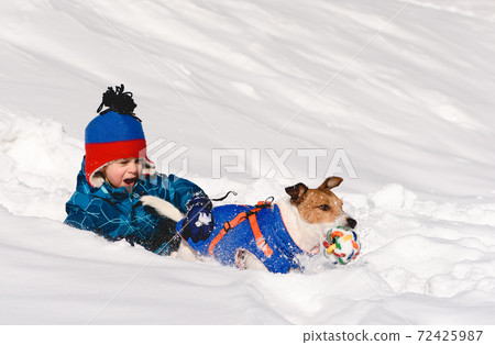 Boy with emotional face expression playing with family pet dog in snow on winter day 72425987