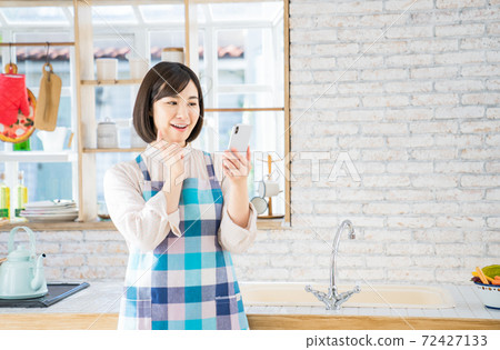 A young woman using a smartphone in the kitchen 72427133