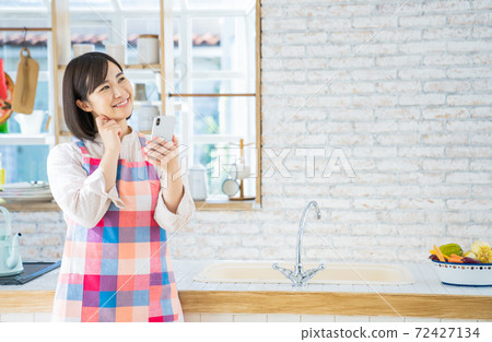 A young woman using a smartphone in the kitchen 72427134