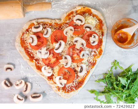 Heart shape pizza dough with tomato sauce and mushrooms preparation 72429827