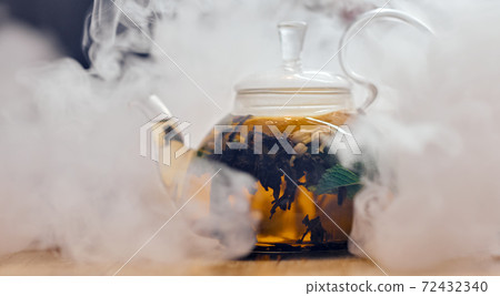 kettle full of tea in puffs of smoke on a wooden table kettle full of tea in puffs of smoke on a wooden table 72432340