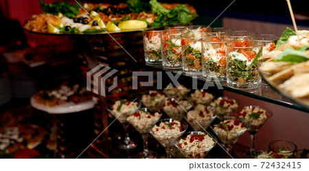 Catering. Glasses with salads and snacks on glass shelves.  72432415