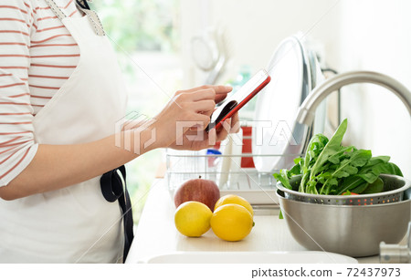 Hands of a woman looking at a smartphone in the kitchen 72437973