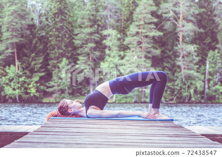 Young yogi girl practicing yoga, Glute Bridge exercise, dvi pada pithasana pose on the lake. Concept of healthy life and natural balance Young yogi girl practicing yoga, Glute Bridge exercise, dvi pada pithasana pose on the lake. Concept of healthy life and natural balance 72438547