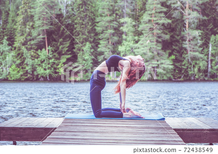 Young yogi girl practicing yoga, stretching in Ustrasana exercise, Camel pose, on the lake. Concept of healthy life and natural balance Young yogi girl practicing yoga, stretching in Ustrasana exercise, Camel pose, on the lake. Concept of healthy life and natural balance 72438549