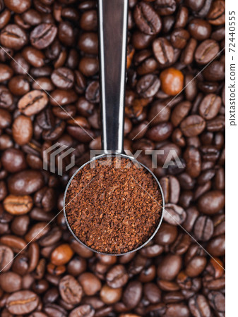 Fresh raw organic coffee powder in silver steel scoop on top of coffee beans. 72440555