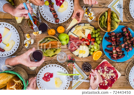 Top view of christmas celebration wooden table full of food decorations and people having fun together - family tradition and friends having lunch or dinner for xmas at home or restaurant Top view of christmas celebration wooden table full of food decorations and people having fun together - family tradition and friends having lunch or dinner for xmas at home or restaurant 72443450