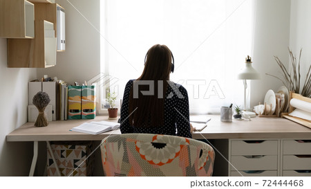 Rear view woman wearing headphones sitting at desk at home 72444468