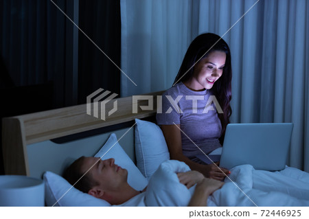 Woman sitting on bed in the night and using laptop computer Woman sitting on bed in the night and using laptop computer 72446925