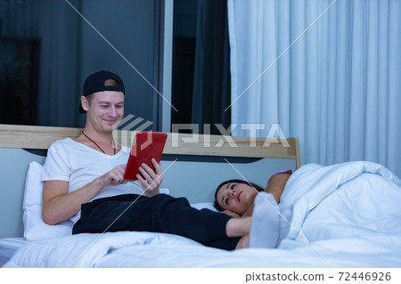 Man sitting on bed in the night and using tablet Man sitting on bed in the night and using tablet 72446926