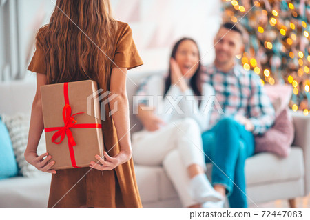 Back view of kid holds a gift box near the Christmas tree indoors. 72447083