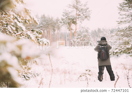 Young Man Backpacker With Photo Camera Taking Photo In Winter Snowy Forest. Active Hobby. Hiker Walking In Snowy Pinewood Forest Young Man Backpacker With Photo Camera Taking Photo In Winter Snowy Forest. Active Hobby. Hiker Walking In Snowy Pinewood Forest 72447101